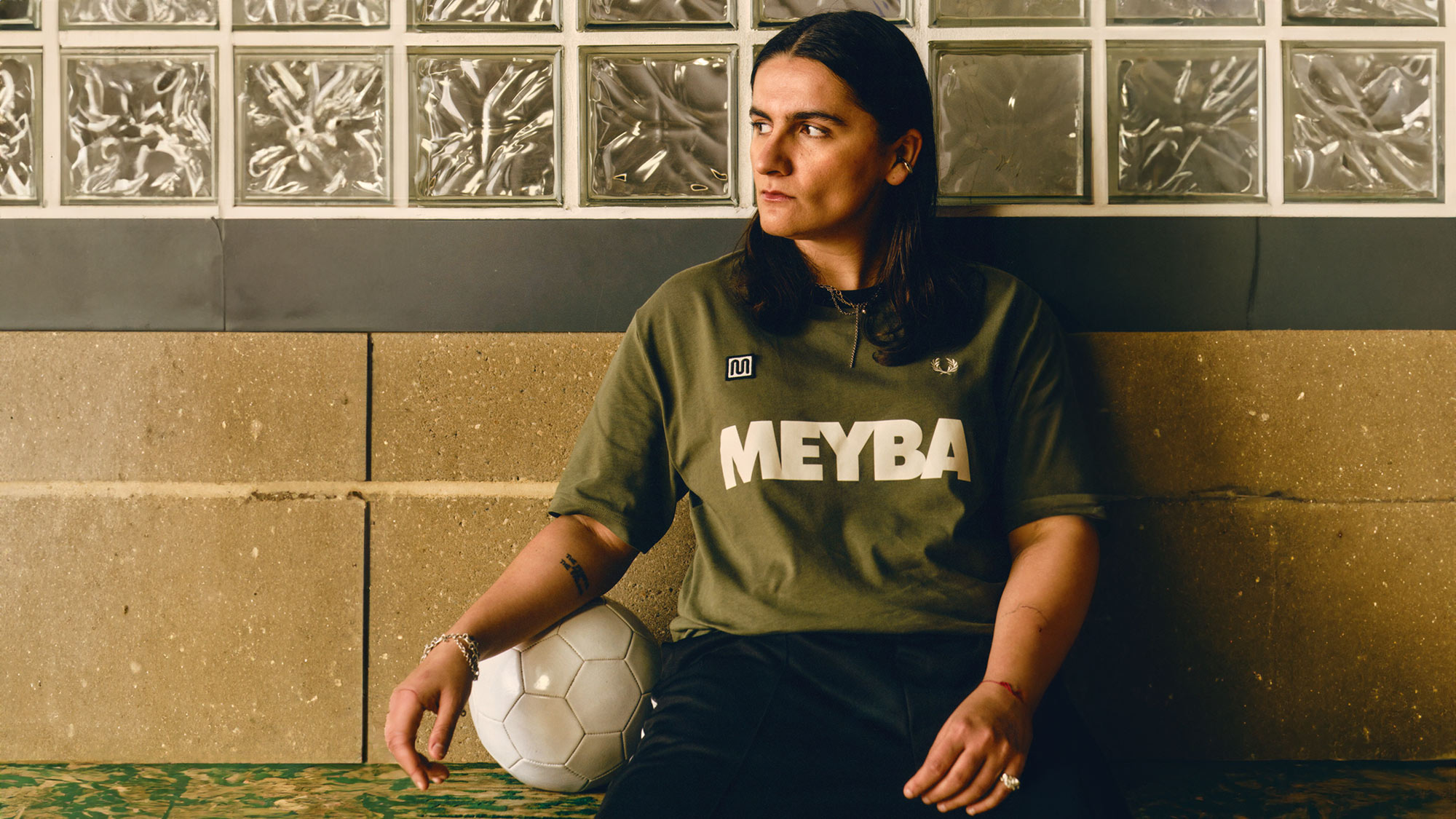 Person wearing olive green sports top sitting on bench holding a football