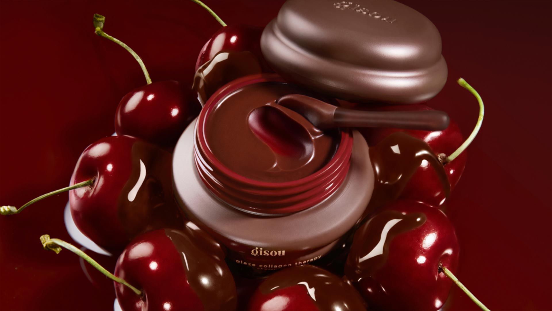 Gisou glass collagen therapy lip mask in jar with applicator, surrounded by fresh red cherries on deep red background