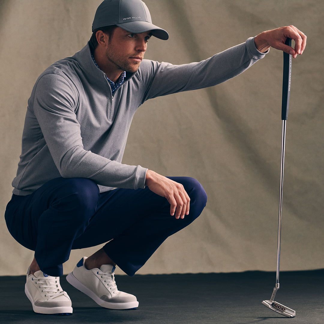 man crouched down with golf club in golf clothes and hat