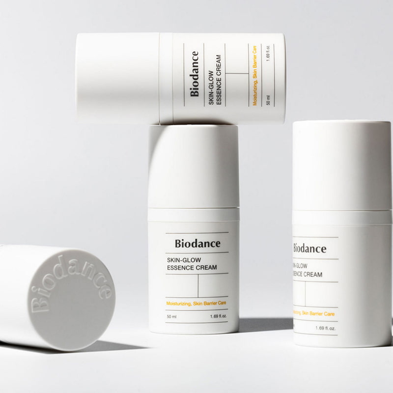 Three white bottles of Biodance Skin-Glow Essence Cream with minimalist design.