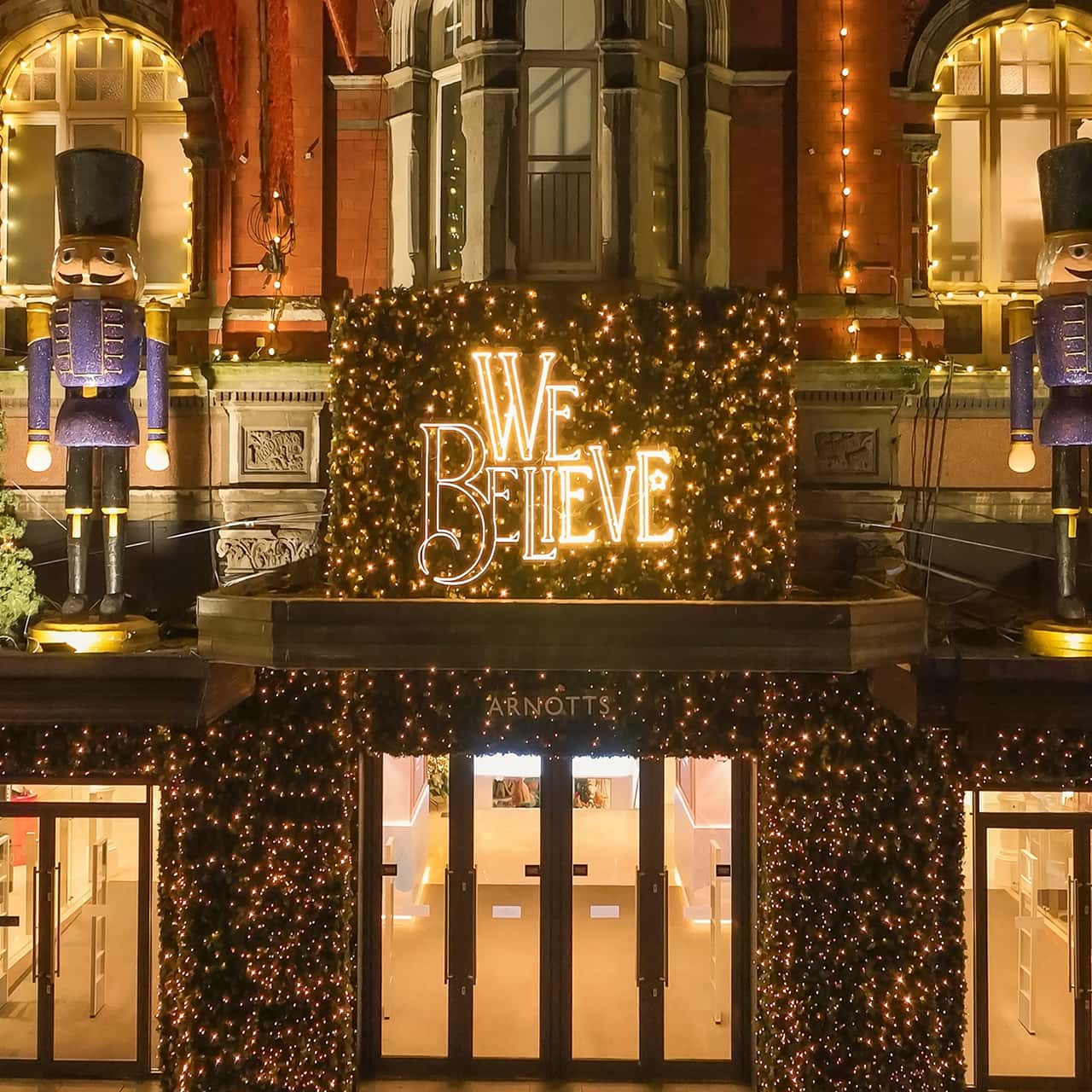 Festively decorated Arnotts storefront with 'We Believe' lights and nutcracker statues on either side, adorned with sparkling lights.
