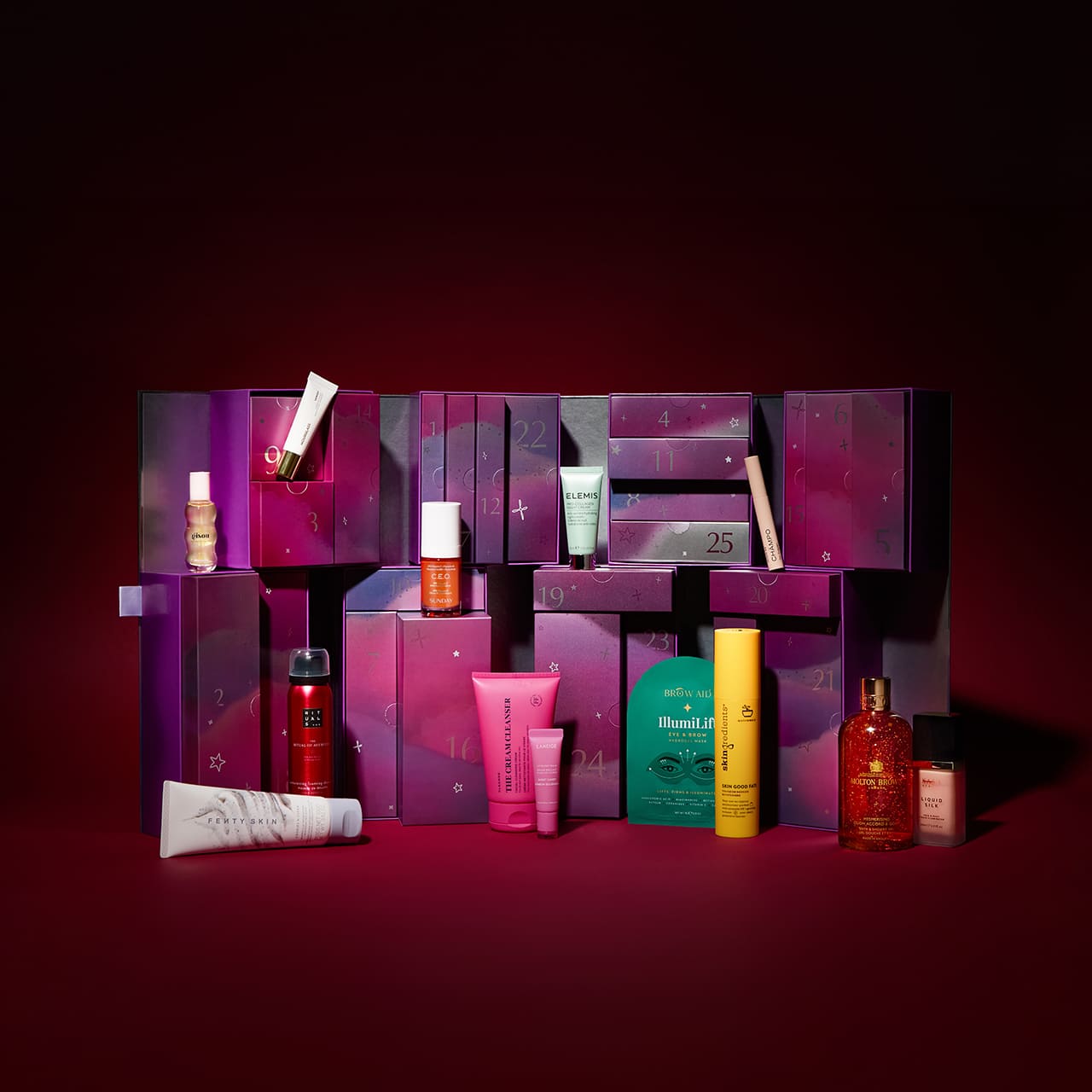 A colorful advent calendar with numbered boxes and various skincare products arranged in front on a dark red background.