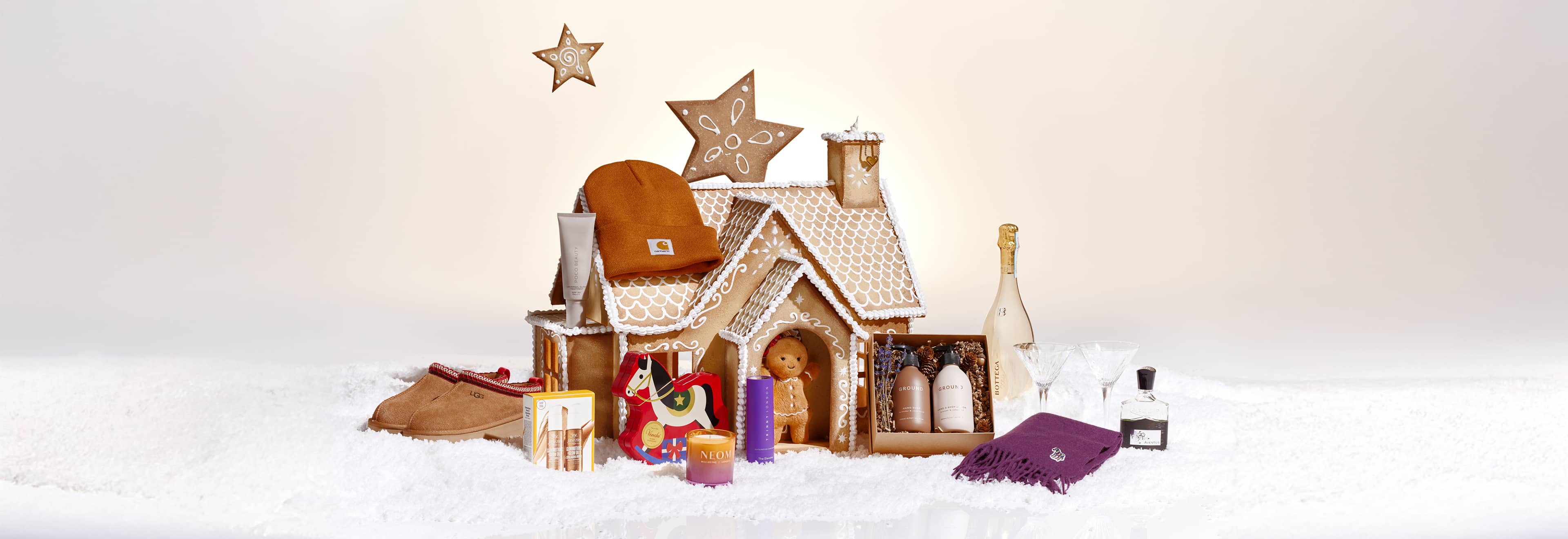 A gingerbread house decorated with stars, surrounded by various gifts and snow.