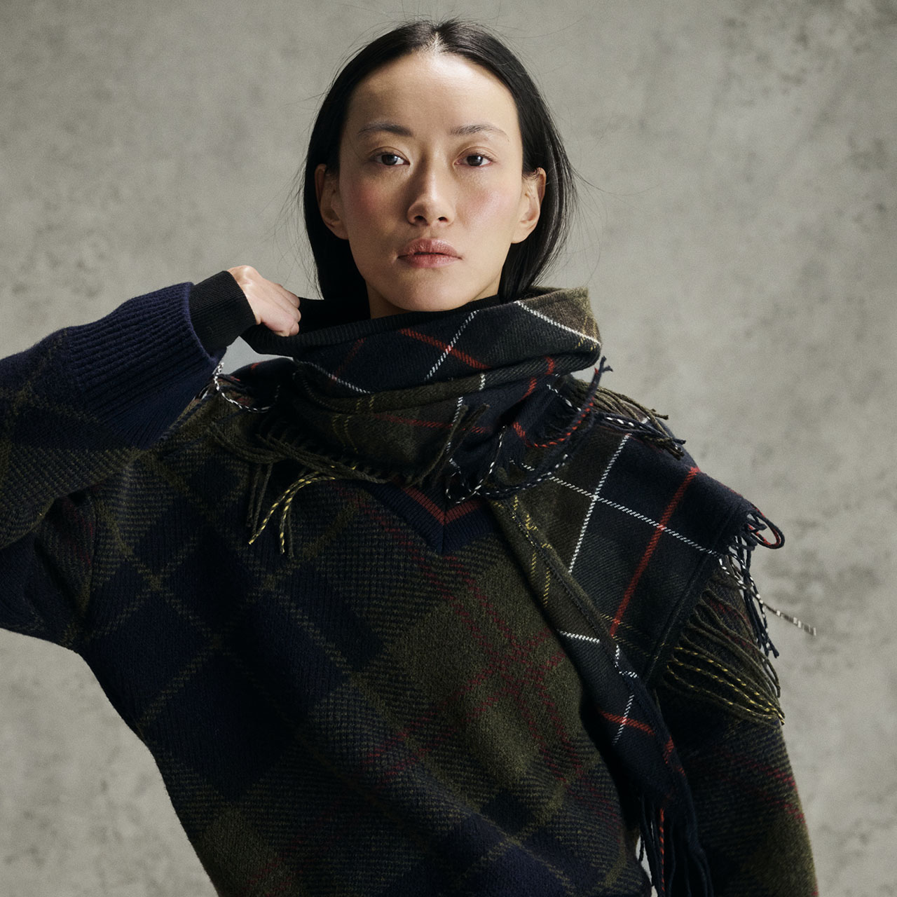 Woman wearing navy knit jumper with tartan scarf in navy, olive and red tones around shoulders