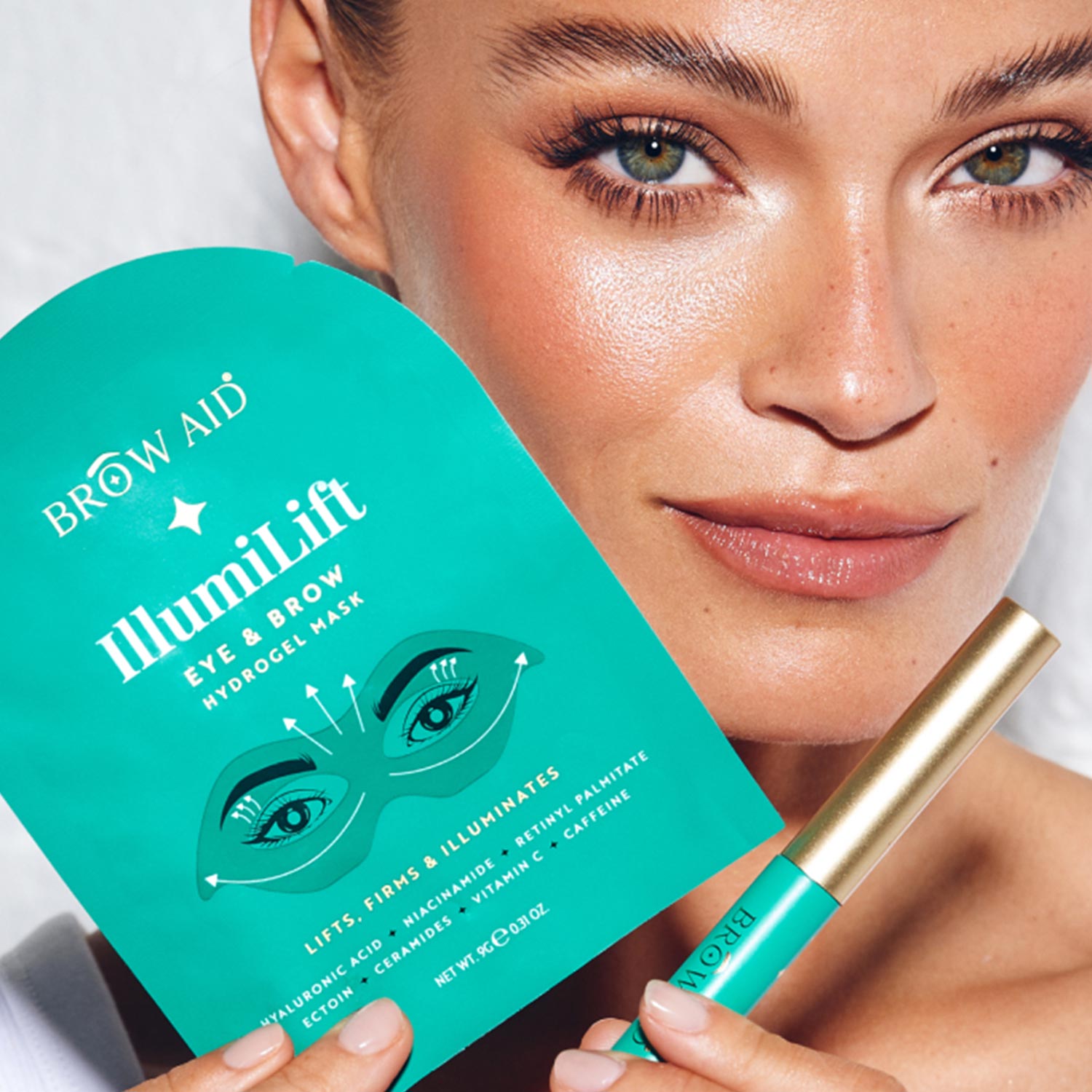 A woman holds an IlluminLift Eye Brow Hydrogel Mask package and a matching cosmetic tube, showcasing eyebrow care products.