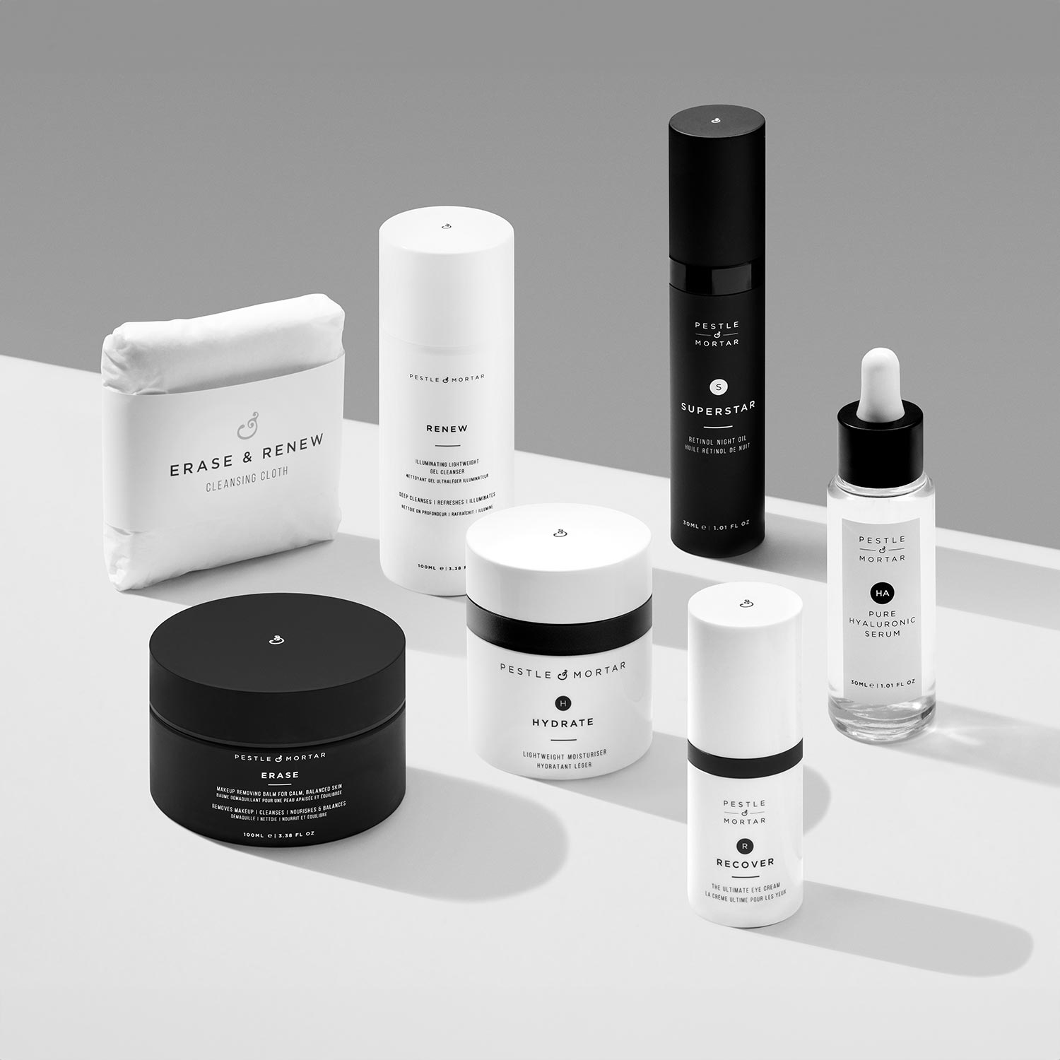 A collection of black and white skincare products, including bottles, jars, and a cleansing cloth, displayed on a gray background.