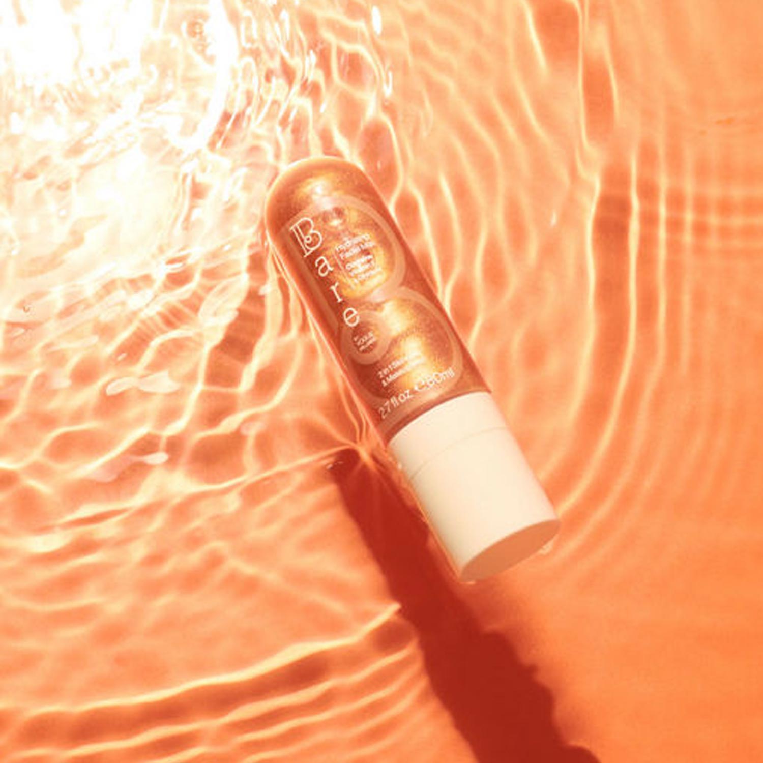 A tube with an orange label floating in shimmering water with a sunlit background.
