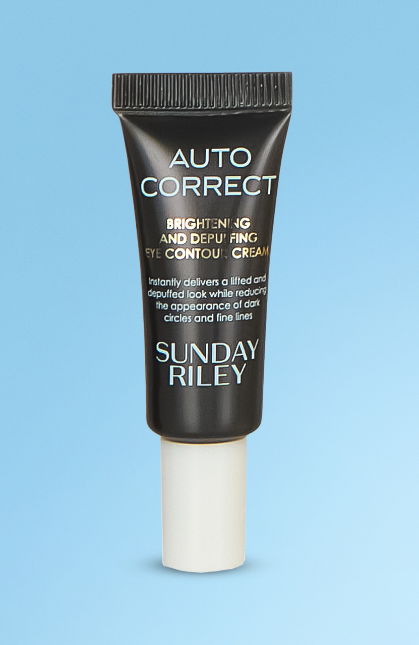 A black tube of 'Auto Correct' eye contour cream by Sunday Riley on a blue background.