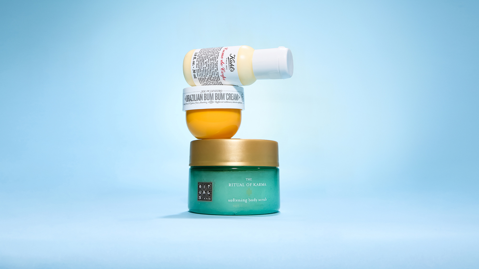 Three skincare products stacked: a bottle on top of a jar labeled 'Brazilian Bum Bum Cream,' which sits on a green jar 'The Ritual of Karma.'