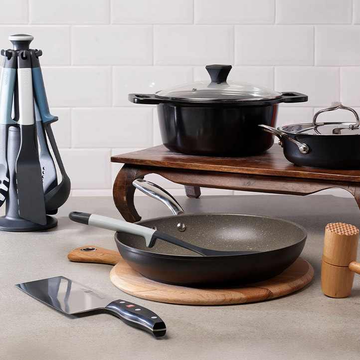 Hard anodised cookware set displayed on stovetop including black frying pan with wooden handle and knife block