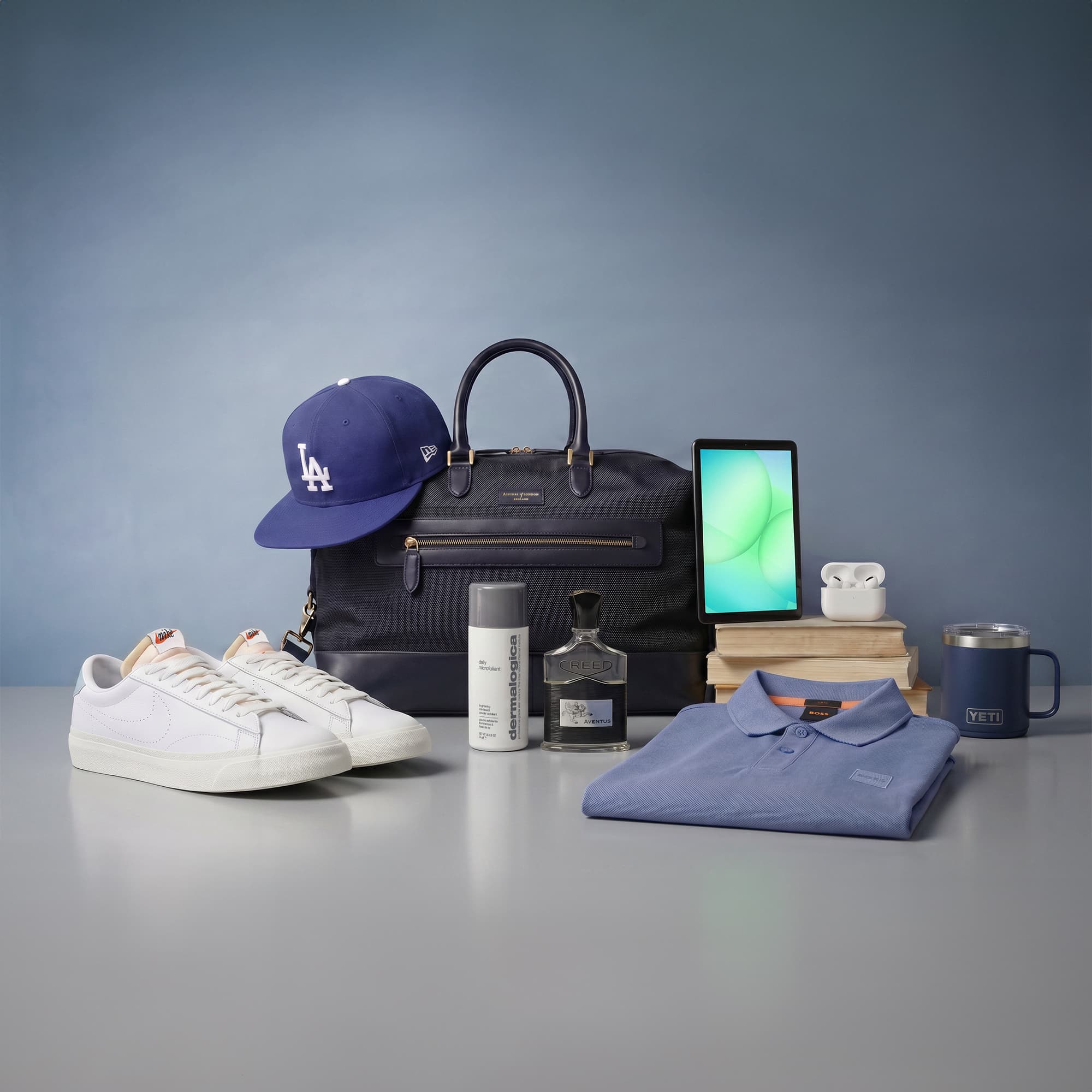 A selection of men's accessories including a bag, cap, shoes, polo shirt, tablet, cologne, AirPods, skincare item, and a mug displayed on a table.