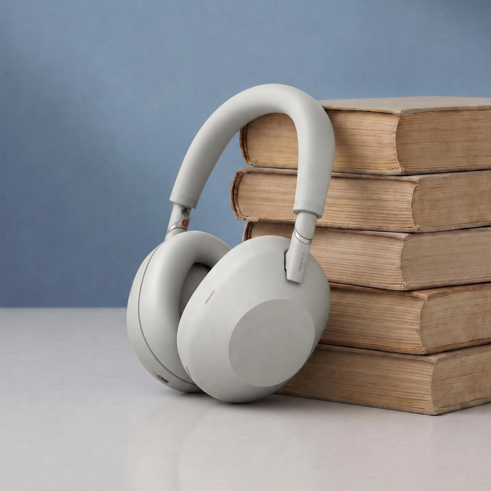 White headphones positioned in front of a stack of five vintage books with brown covers against a plain blue background, symbolising the concept of audiobooks.