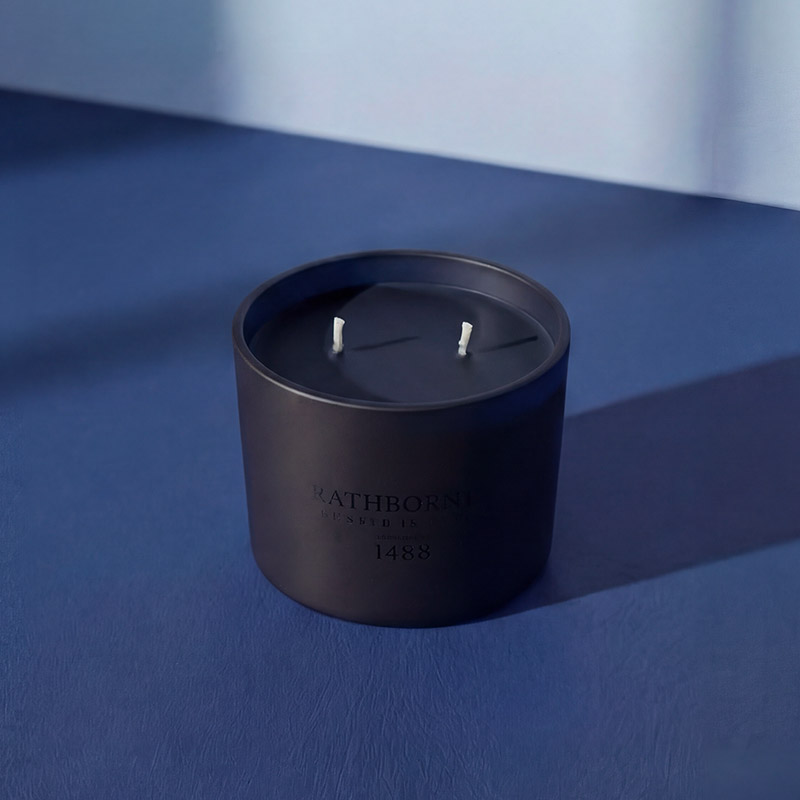 A dark blue Rathbornes candle with two wicks, set against a blue surface and wall.

