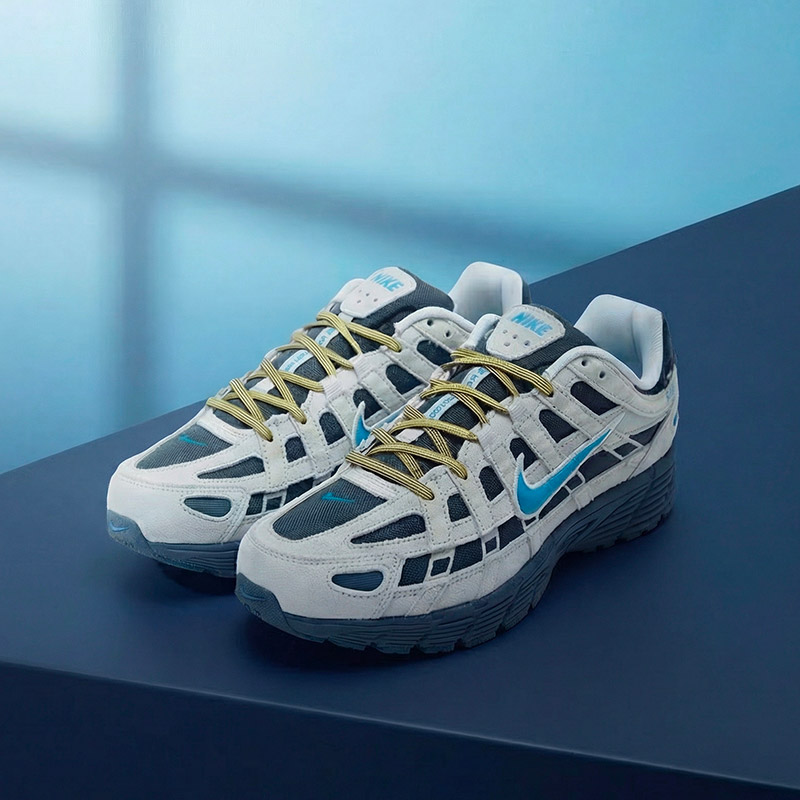 A pair of gray and blue sneakers with yellow laces, featuring a prominent swoosh logo, displayed on a blue surface.