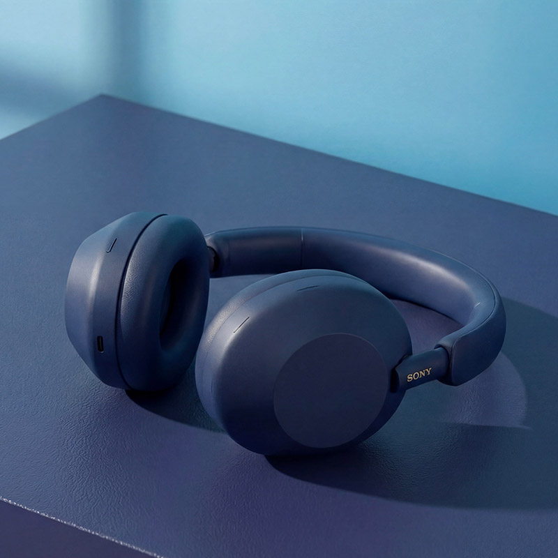 Blue Sony headphones resting on a blue surface against a gradient blue background.