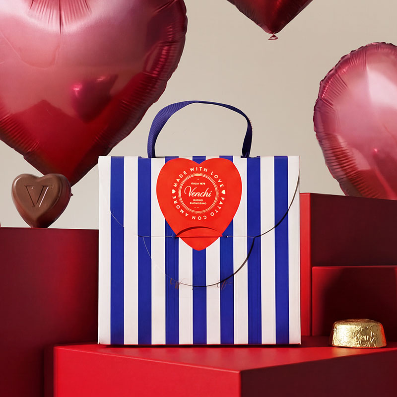 Blue and white striped bag with a red heart, surrounded by heart-shaped balloons and red boxes.