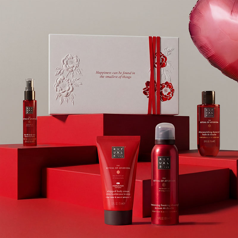 Beauty products on red platforms with a white gift box; a red heart-shaped balloon is on the right.