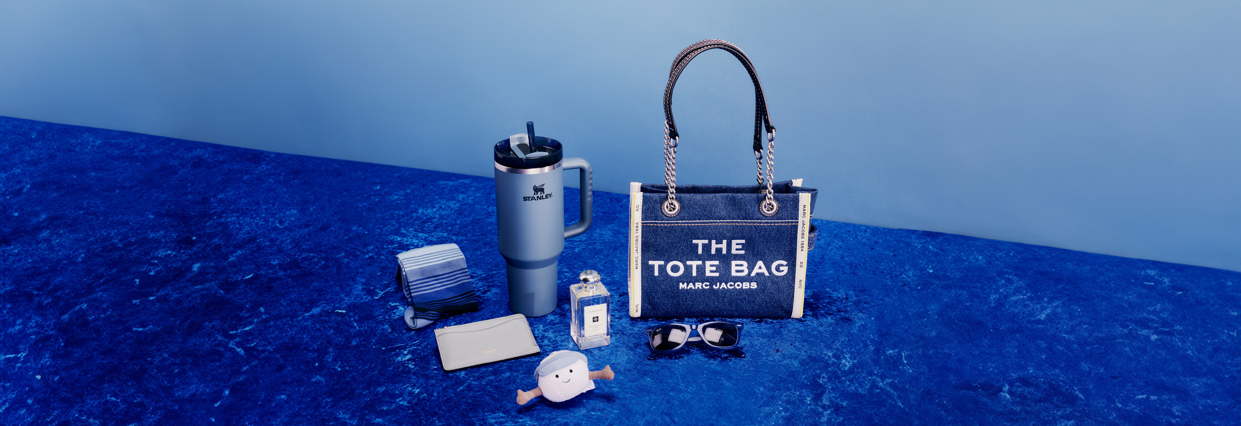 A collection of assorted items including a shoe, mug, plush toy, cap, candle, and skincare products arranged on a green background.