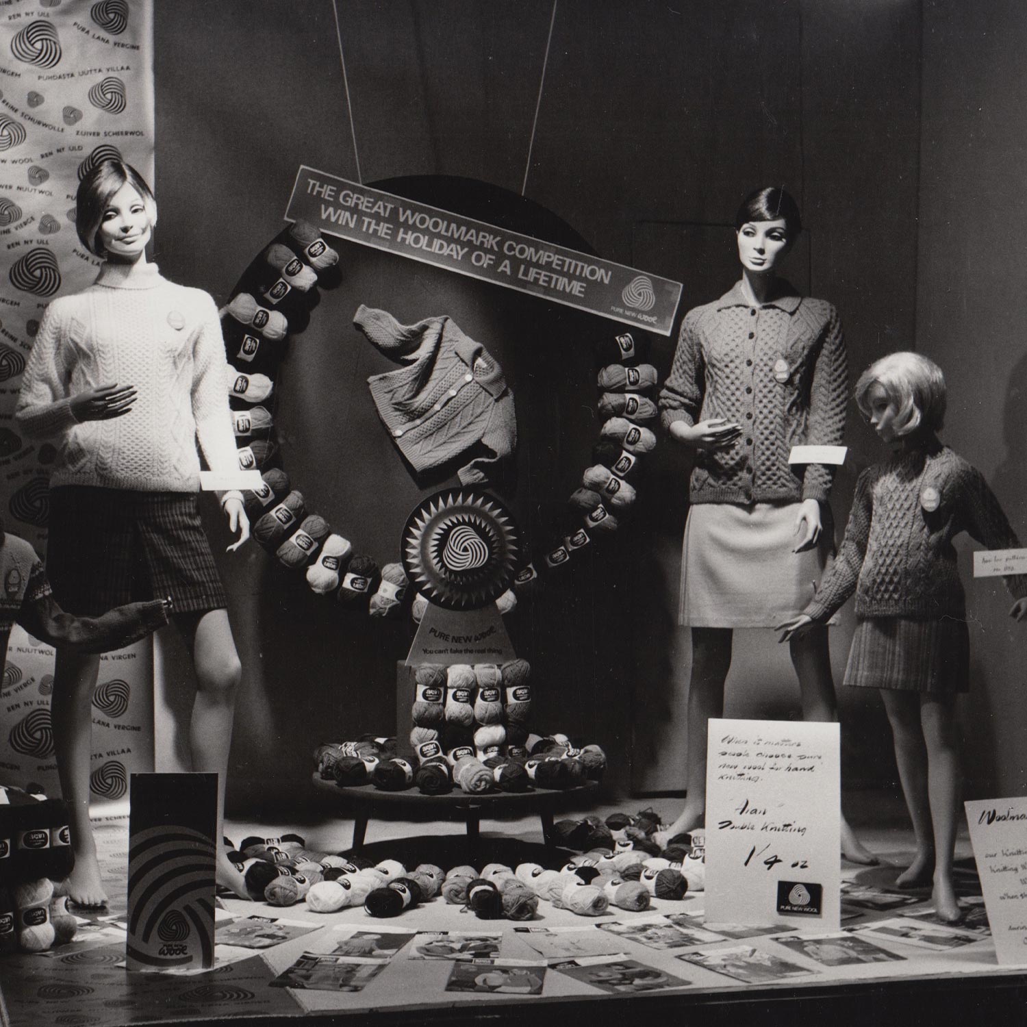 Black and white vintage display of 1950s teenage fashion with models wearing knitted jumpers and skirts surrounded by coloured yarn and competition signage