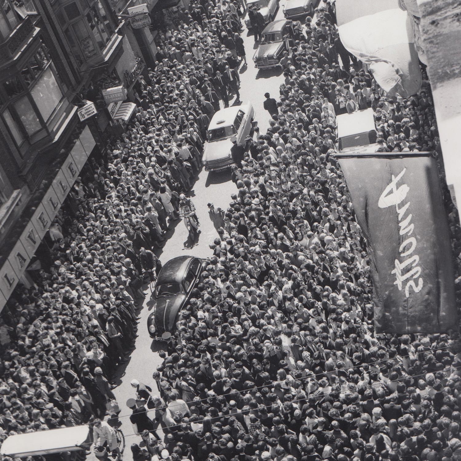 Aerial view of crowded Dublin street lined with crowds and vehicles during celebrity visit, with Arnotts banner visible on right side