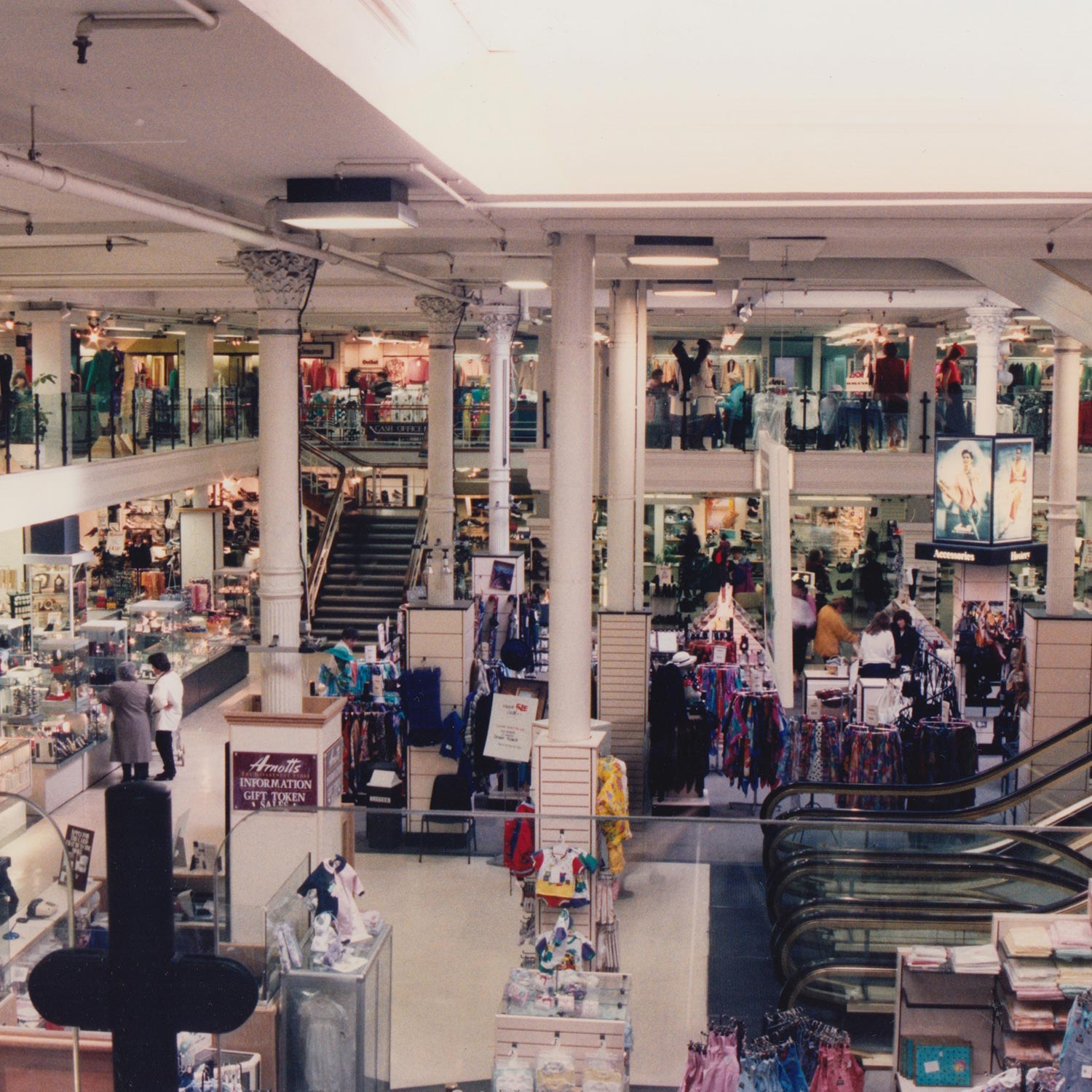 Busy multi-level department store interior with shoppers browsing clothing and accessories across multiple floors.