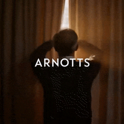 Silhouette of person opening gold curtains to bright window light with Arnotts branding