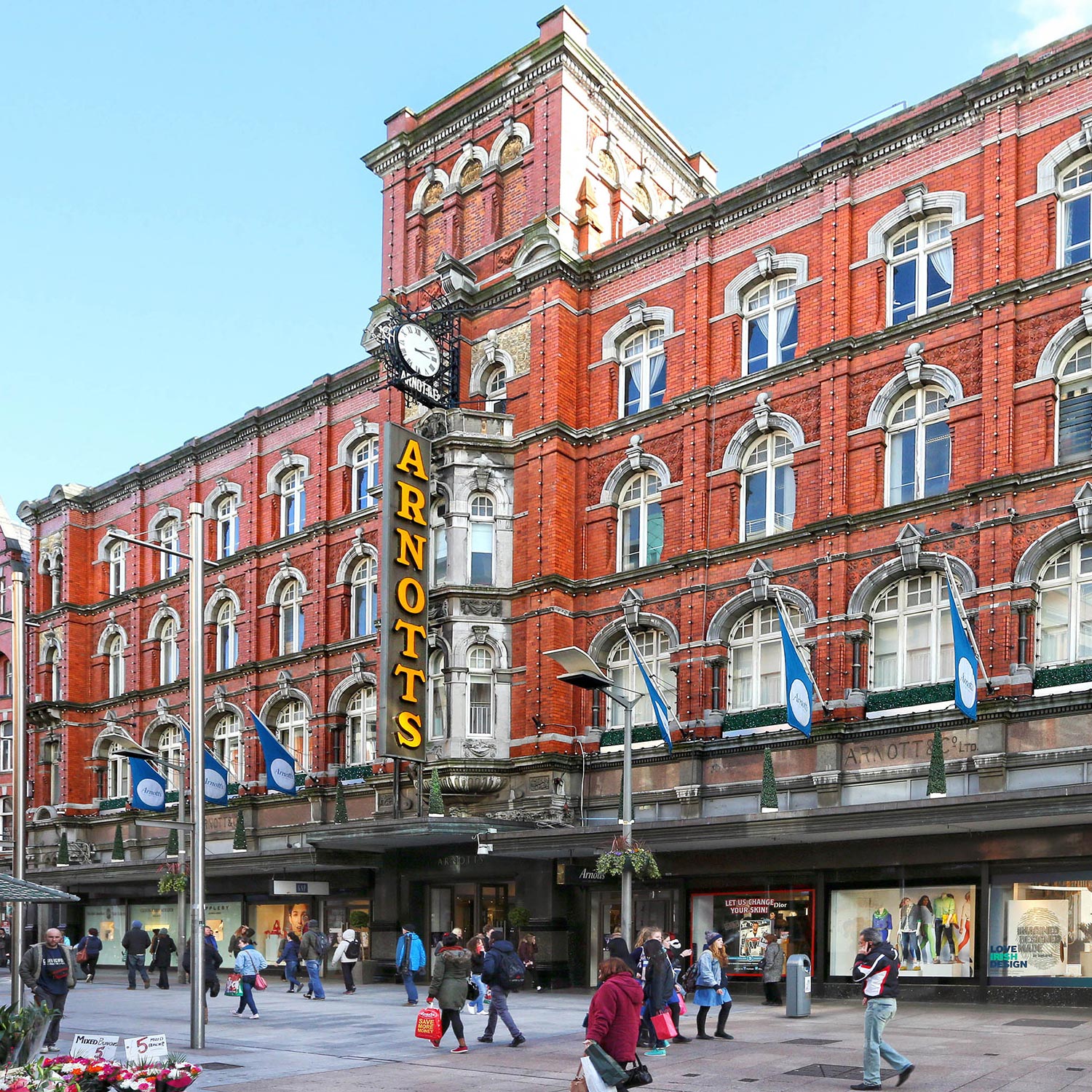 Historic red-brick Arnotts department store building with yellow signage, clock, and shoppers in the street below