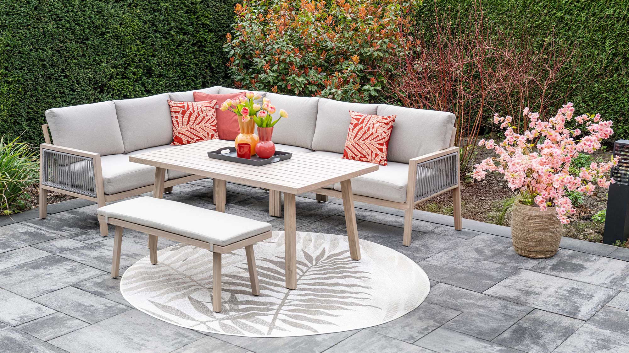 A cozy living room setup featuring a beige sectional sofa, matching ottoman, and wooden side tables, against a paneled wall.

