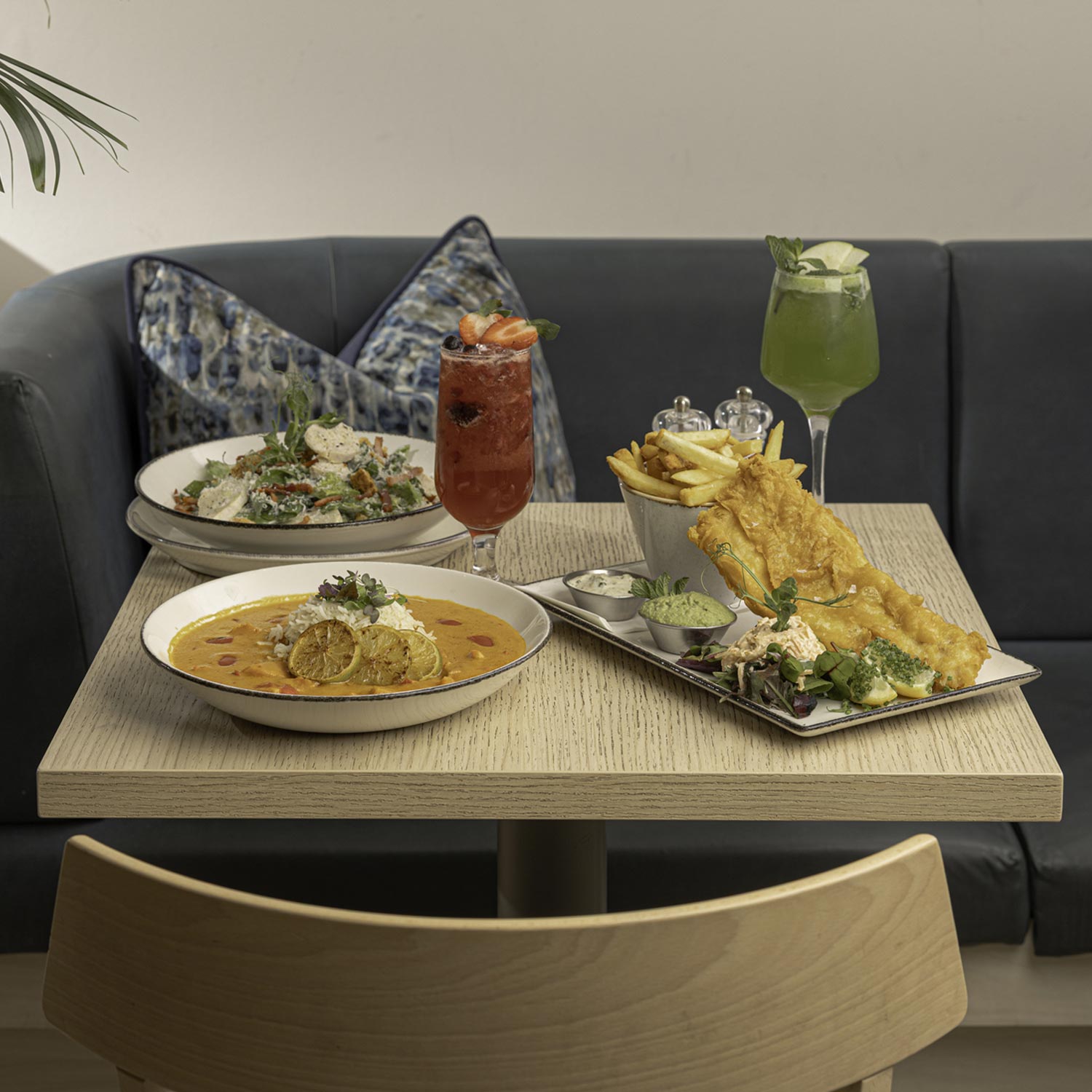 A table with seafood dishes, two colorful drinks, and a stylish, cozy dining setting.
