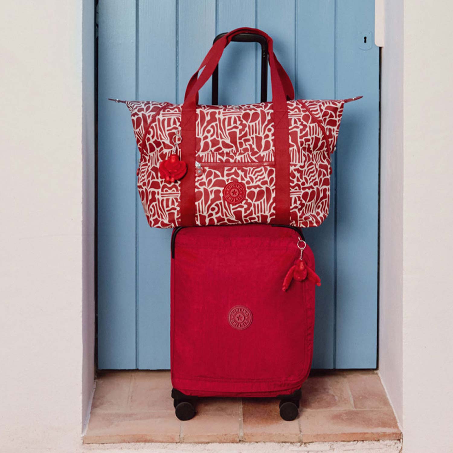 AA red suitcase with wheels and a patterned red bag on top, positioned against a blue wooden door.