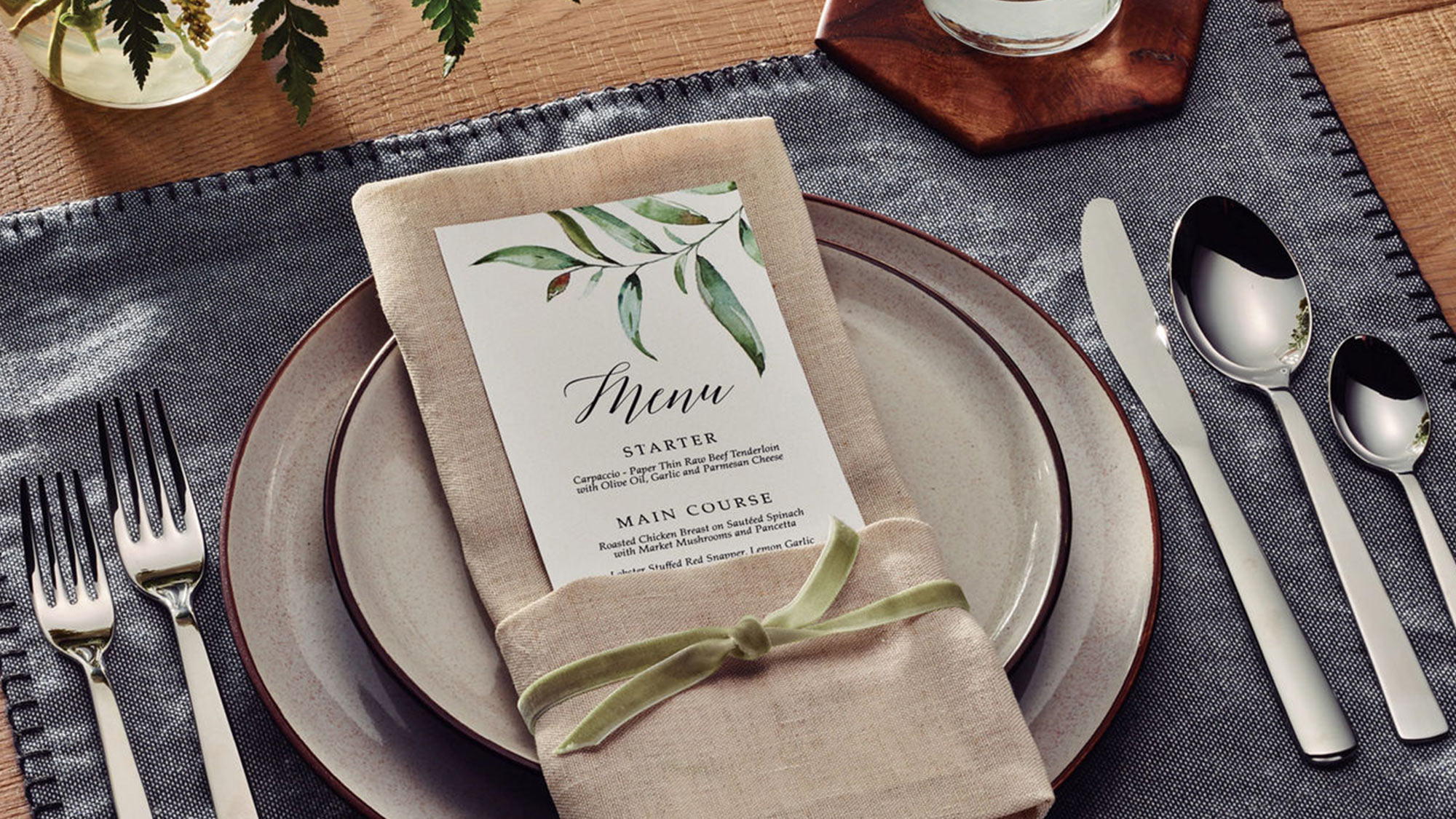 Elegant table setting with a menu on a napkin, surrounded by plates, cutlery, a water glass, and a floral centerpiece.