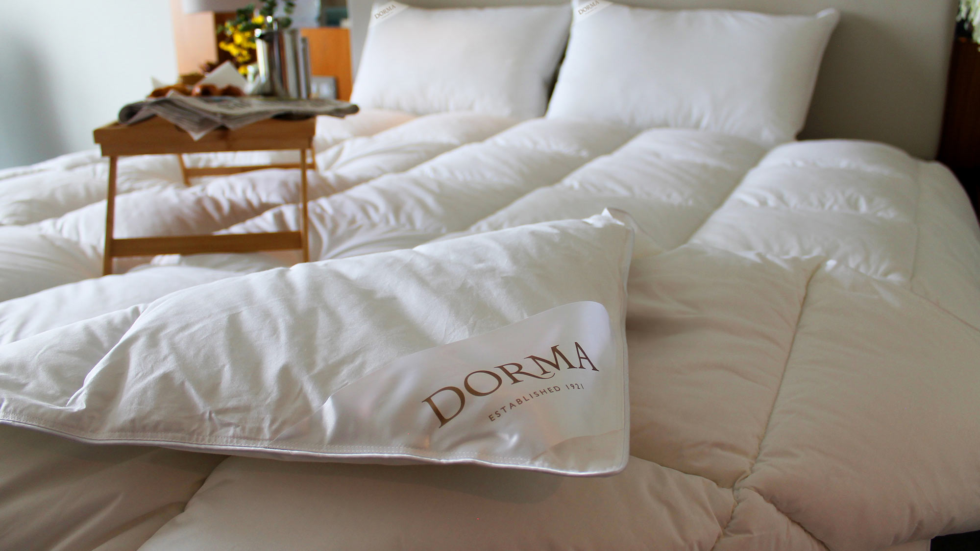 A neatly made bed with white bedding and a 'Dorma' pillow; a wooden breakfast tray sits on the bed.