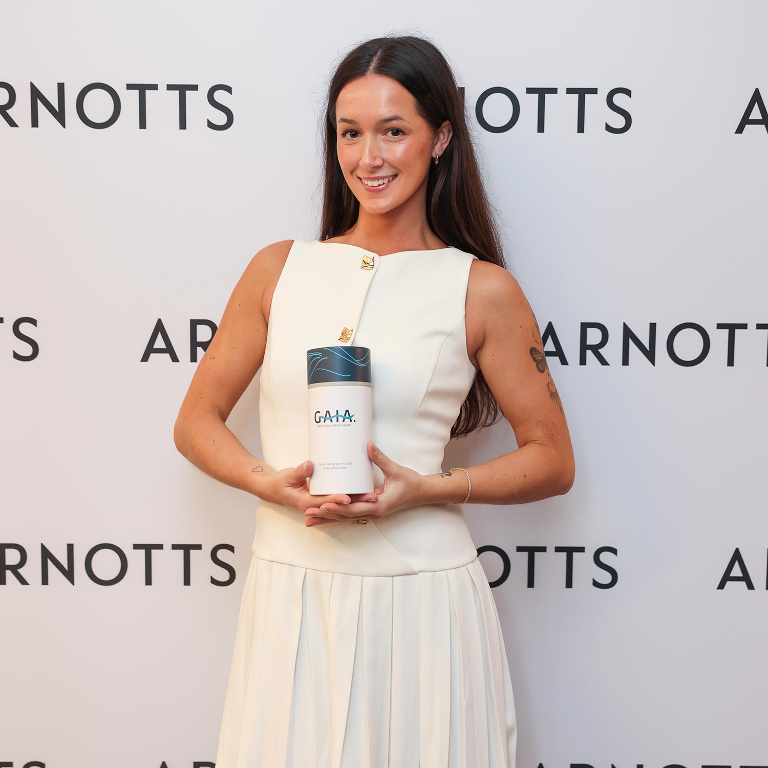 A woman in a white dress holds a product labeled 'GAIA' in front of an Arnotts-branded backdrop.