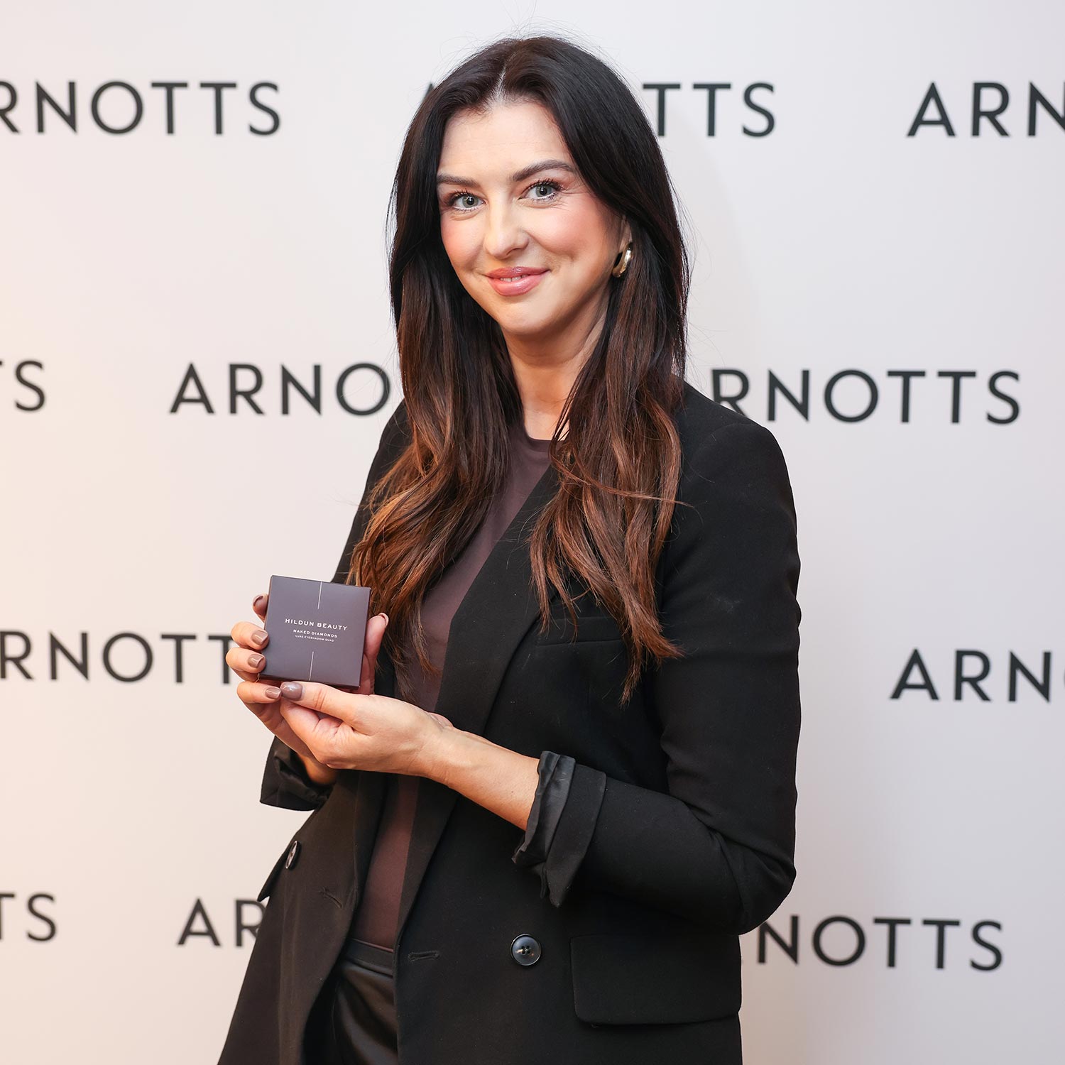 A person holding a product stands in front of an Arnotts branded backdrop, smiling.