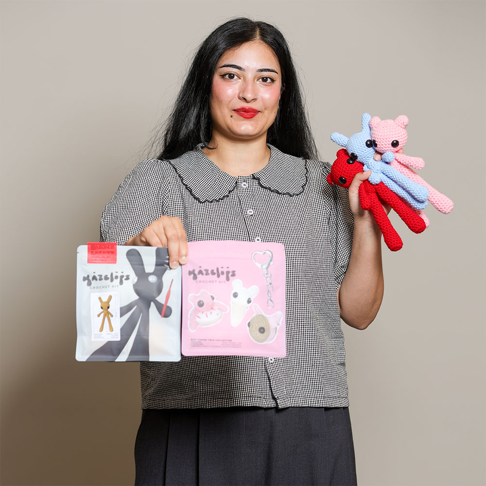 Woman holding Kazclops crochet kits and crocheted colourful character creatures in pink, red and blue