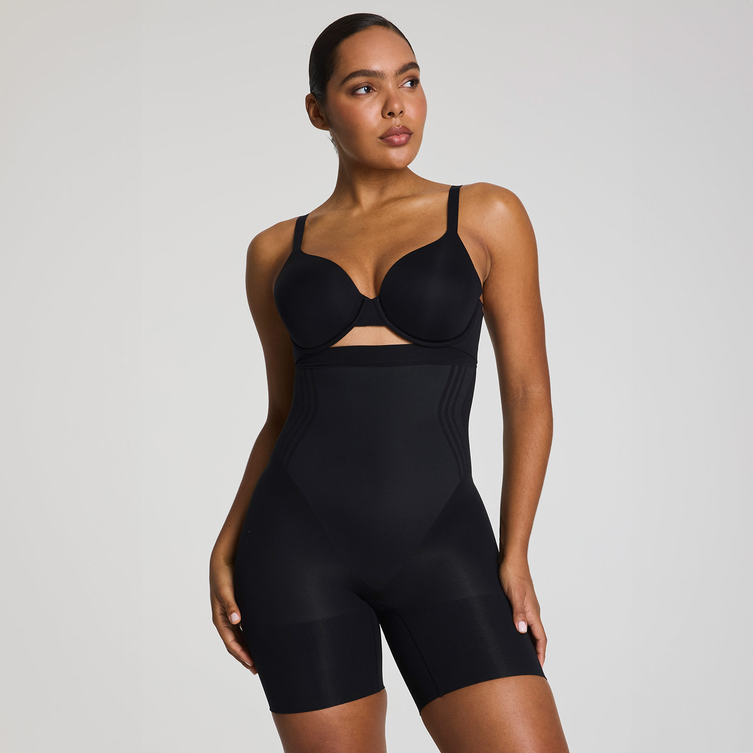 A person sits on a chair, wearing a white top and black pants, resting their head on their hand.