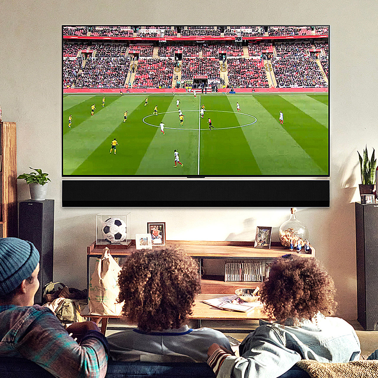 People sitting on a couch, watching a soccer match on a large TV in a cozy living room.