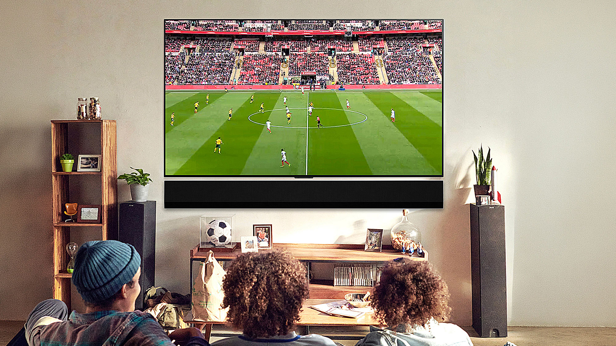 Three people on a couch watching a soccer match on a large TV in a living room.