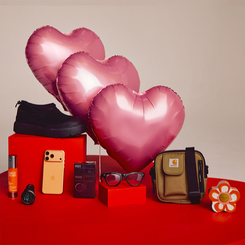 A display of pink heart-shaped balloons with various items including a shoe, smartphone, glasses, and a small bag on a red surface.