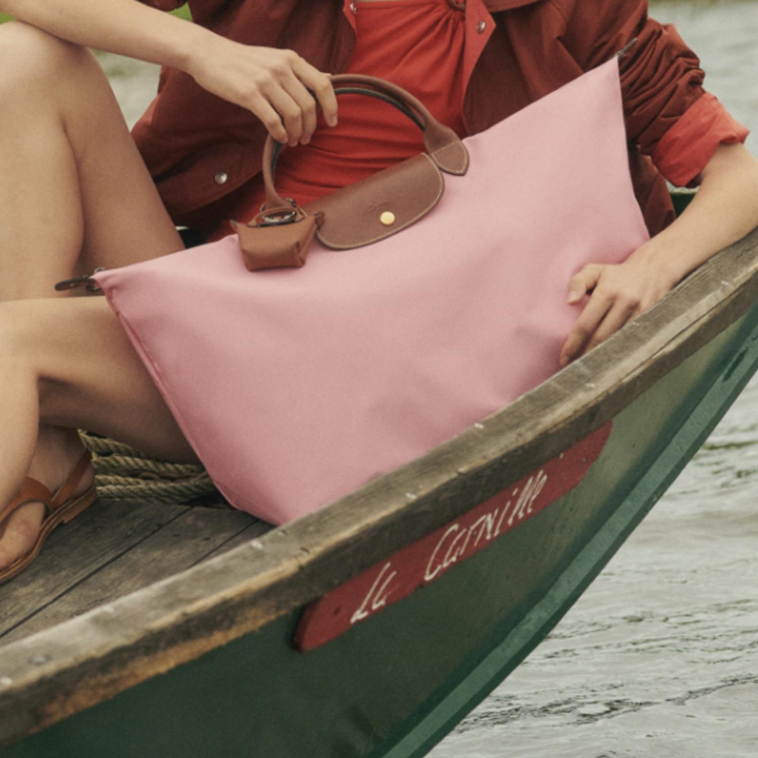 A person in a boat holds a pink handbag and wears a red outfit.