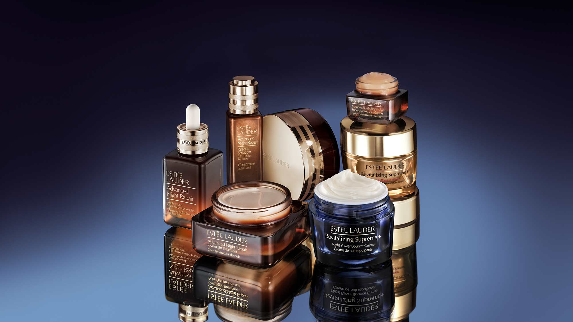 A collection of Estée Lauder skincare products displayed on a reflective surface with a dark gradient background.