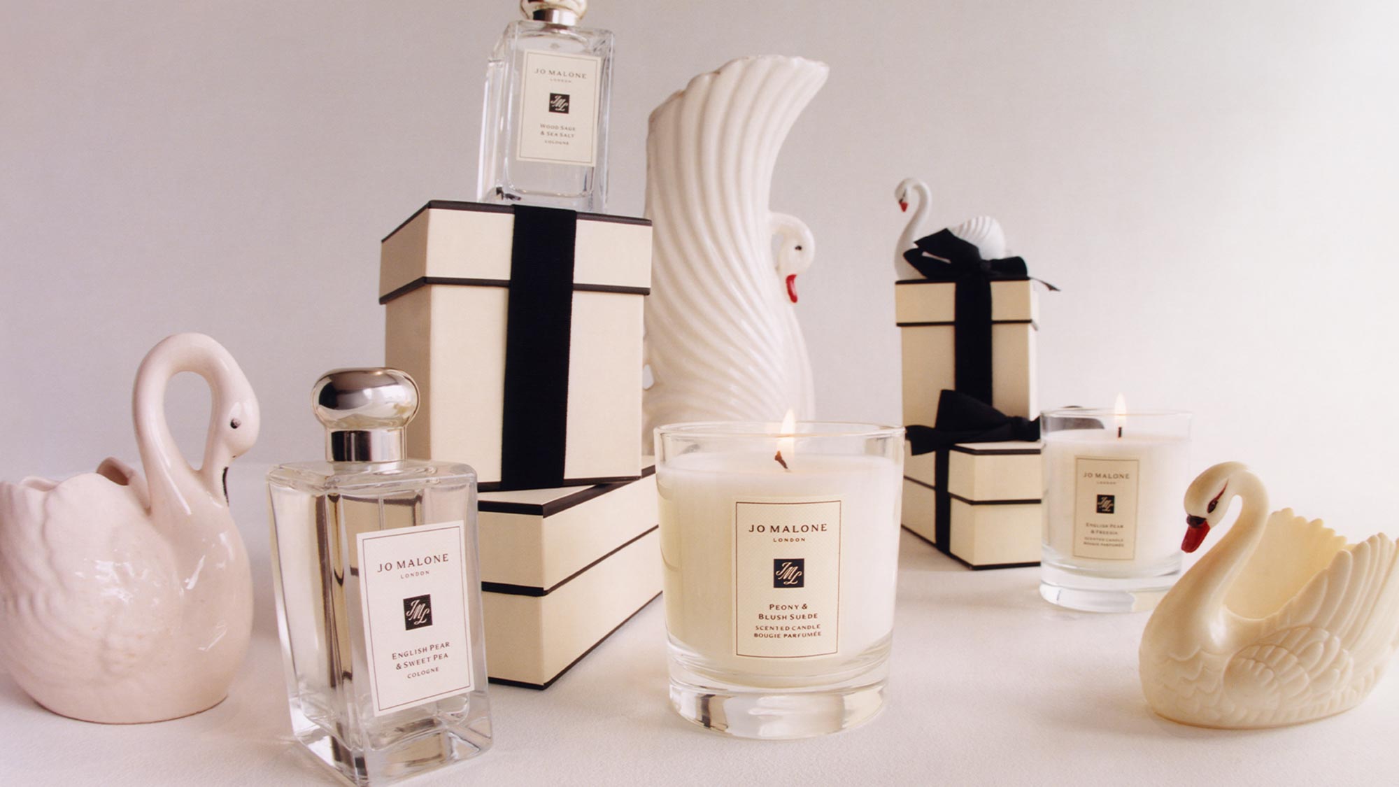 Perfume bottles and candles with swan decorations and gift boxes in a soft, elegant setting.