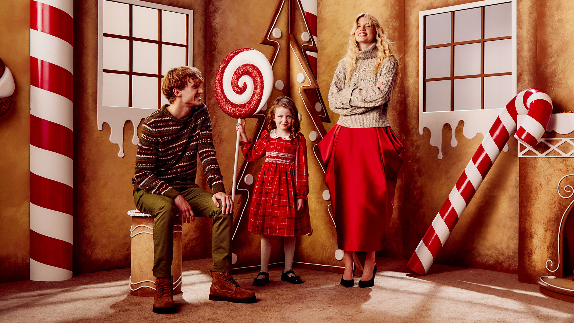 A family in a gingerbread-themed room with candy decorations and holiday attire.