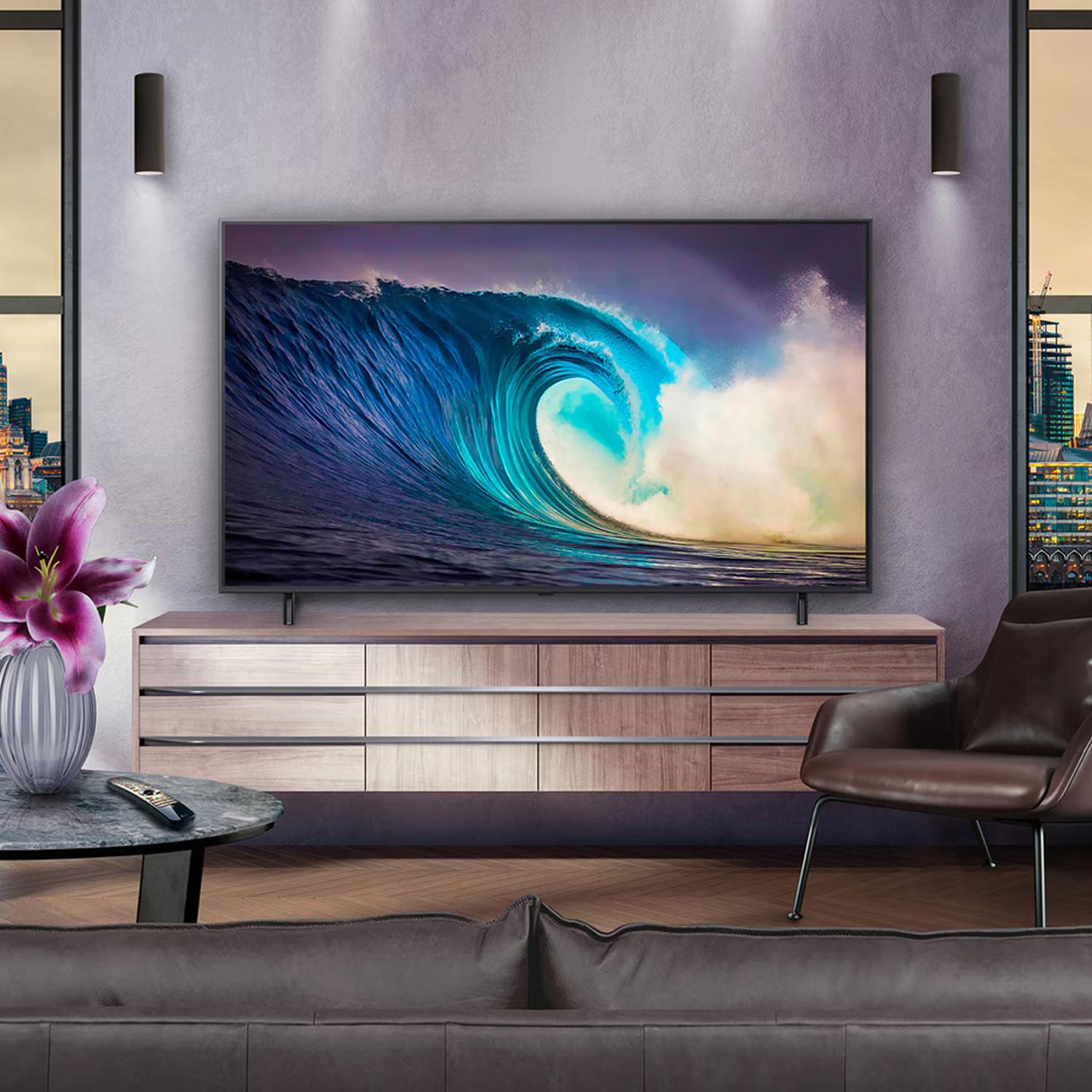 Modern living room with a large TV displaying a wave, purple flowers on a table, leather chair, and cityscape view.