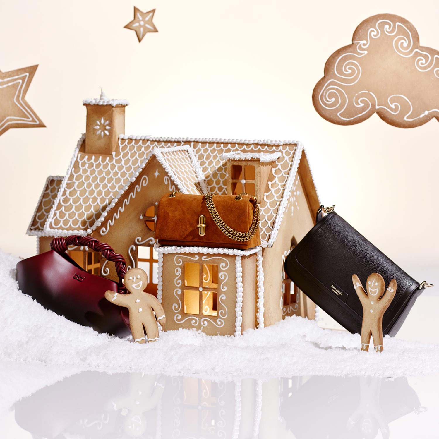 Gingerbread house scene with star and cloud decorations, featuring handbags and gingerbread figures on snowy ground.