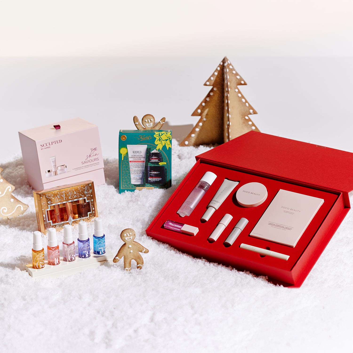 Holiday-themed beauty gift sets displayed on white snow with gingerbread figures and decorative trees.