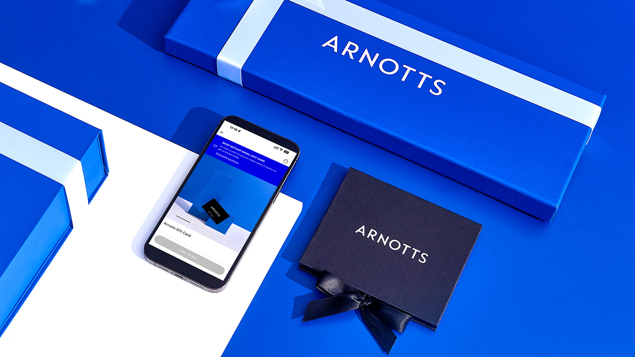 Blue gift boxes with 'ARNOTTS' branding, a smartphone displaying a screen, and a small black ribbon-wrapped box on a blue background.