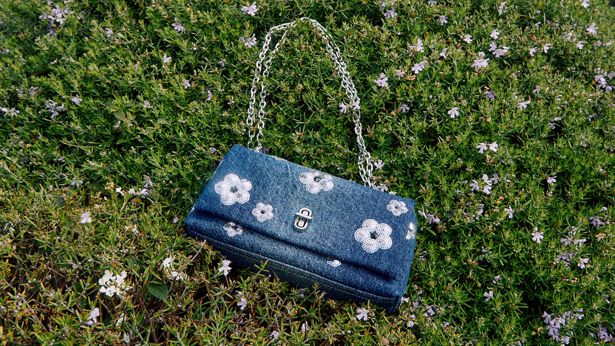 marc jacobs denim handbag with white detailed flowers laying on the grass