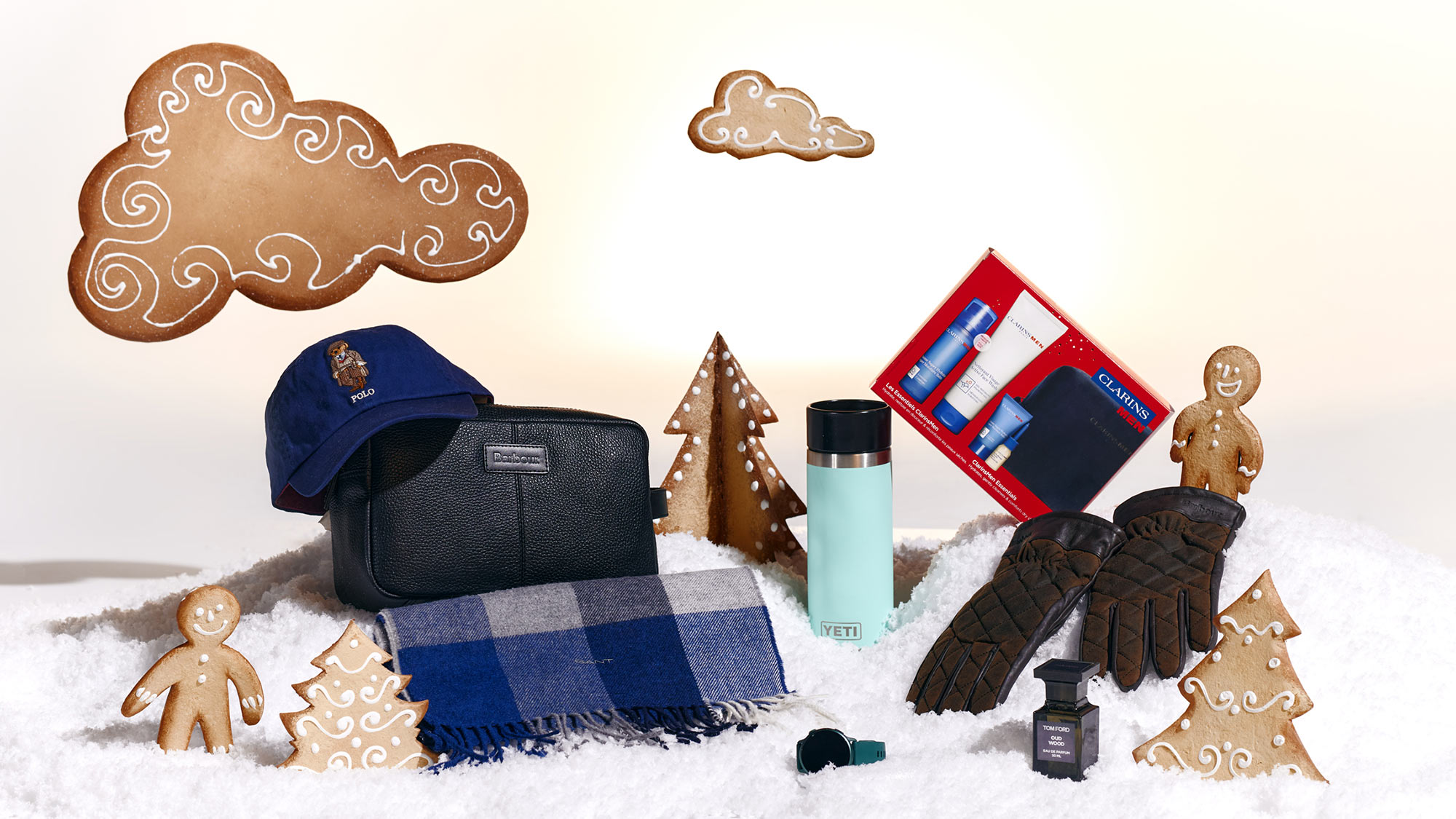 Winter-themed display with a blue cap, scarf, gloves, thermos, toiletry kit, and gingerbread decorations on faux snow.