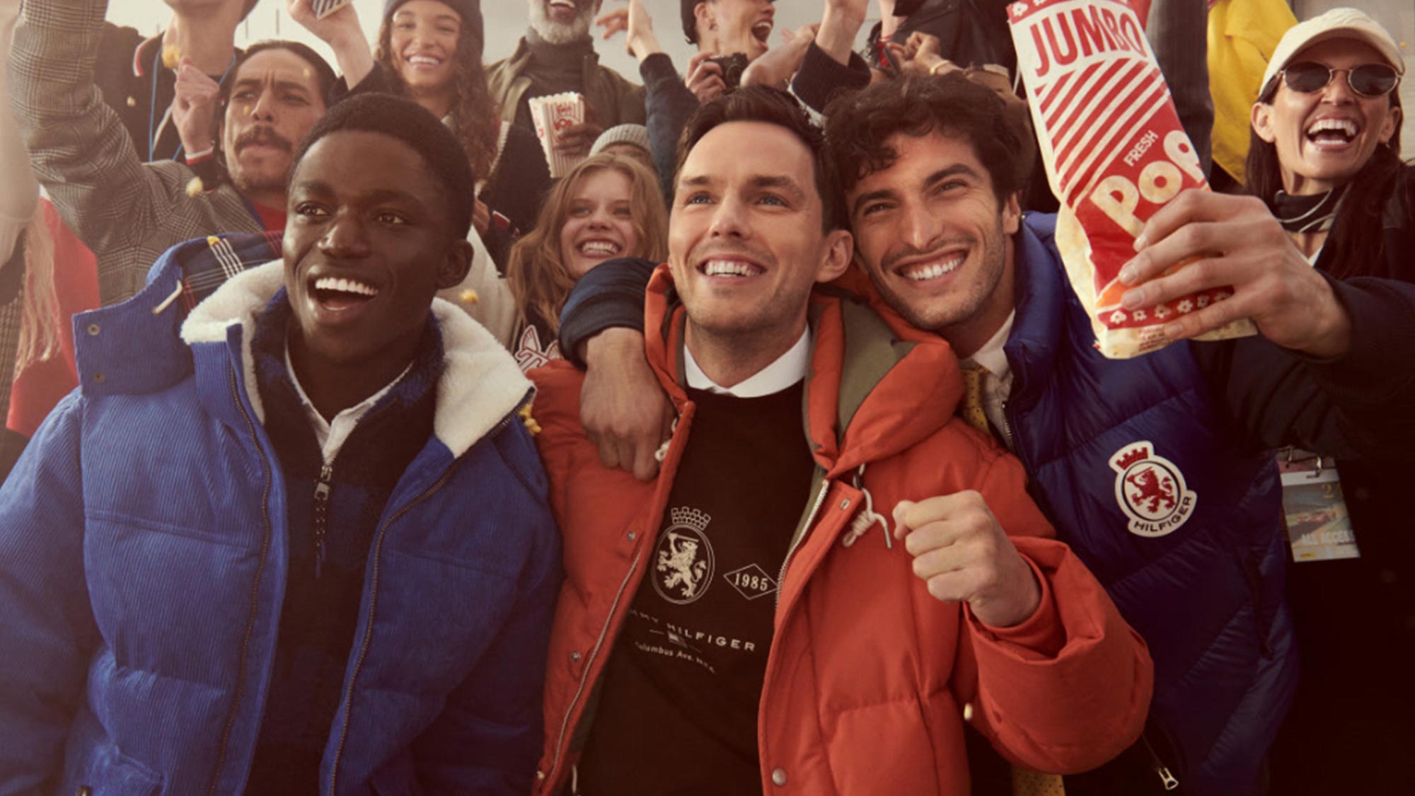 A diverse group of excited people, wearing colorful winter jackets, celebrate together holding popcorn, with a festive atmosphere.